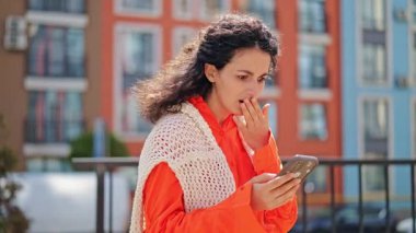 Havalı turuncu elbiseli üzgün bir kadın dışarıdaki kötü haberlere tepki veriyor. Şok, umutsuzluk, keder hisseden şık bir kadın, şehirdeki akıllı telefondan mesaj okuyor..