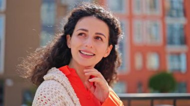 Bej örülü hırka ve turuncu gömlekli güzel, neşeli bir kadın gülümsüyor ve yüzünü çeviriyor, güneşli bir günün tadını çıkarıyor..