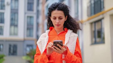 Endişeli iş kadını telefon başında kötü haber okuyor. Turuncu elbiseli şık iş kadını şehir sokaklarında kaygısını dile getiriyor.