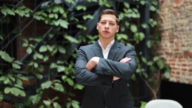 Takım elbiseli kendine güvenen işadamı modern ofiste kollarını kavuşturmuş duruyor. Profesyonellik ve başarı yayıyor..