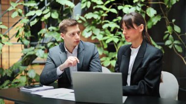 Resmi giyimde odaklanmış meslektaşlar, dizüstü bilgisayar ve belgeler kullanarak ofiste bir projeyi tartışıyorlar. Hevesli iş ortakları bir strateji geliştirir, fikirleri paylaşırlar..