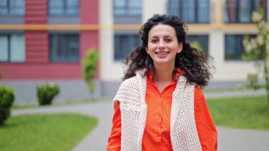 Kameraya gülümseyen şık kıyafetli neşeli esmer bir kadının portresi. Modern mimarinin önünde güneşli bir günün tadını çıkaran bir kız. Modern Mimarinin Önünde Neşeli Esmer