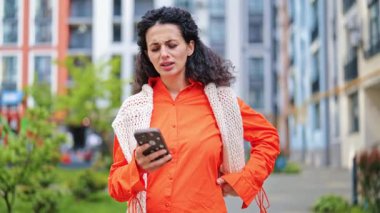 Parlak kıyafetler giymiş şık bir kadın, şehirde akıllı telefon kullanıyor. O, stresten rahatlamaya çeşitli duygular tecrübe eder..