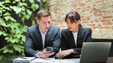 Projeye odaklanmış iş adamları. İş kadını ve işadamı resmi olarak giyinme stratejisini modern ofiste dizüstü bilgisayar ve akıllı telefon kullanarak tartıştılar.