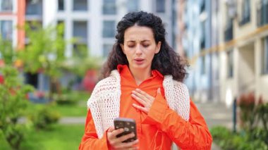 Endişeli kadın telefonda kötü haber okuduktan sonra göğüs ağrısı ve panik hisseder. Portakallı ve telefonlu şık bir kadın. Stres, sağlık, kötü haber..