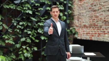 Takım elbiseli kendine güvenen bir iş adamı. Başarılı yatırımcı, bitkilerle modern ofiste mutlu ve tatmin olmuş bir şekilde duruyor..