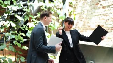 Heyecanlı iş ortakları başarılı anlaşmayı kutluyor. Takım elbiseli neşeli işadamı ve iş kadını modern ofis koridorunda dans edip gülüyorlar..