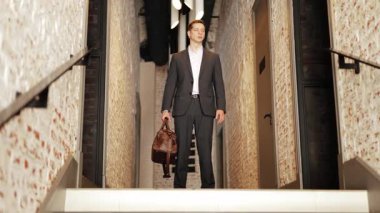 Takım elbiseli kendine güvenen işadamı bir ofis koridorunda elinde bir çantayla duruyor. Profesyonellik ve kararlılık sergiliyor..