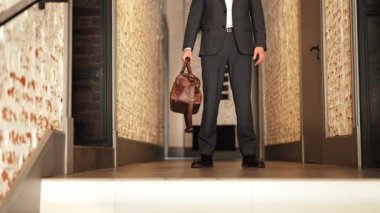 Takım elbiseli kendine güvenen işadamı, elinde deri bir çantayla ofis koridorunda duruyor. Profesyonellik ve başarı yayıyor..