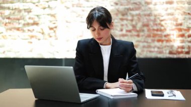 Resmi giyinmiş iş kadını çevrimiçi toplantı sırasında notlar alır. Modern ofis alanındaki görevleri ustalıkla yönetir..