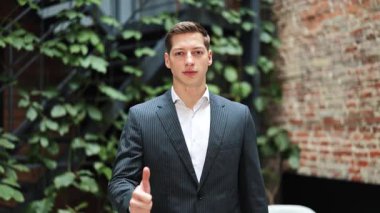 Takım elbiseli kendine güvenen işadamı onaylıyor. Başarılı yatırımcı, modern ofiste tesisleri olan tuğla duvarın yanında duruyor. Neşeli adam iyi işi destekliyor..