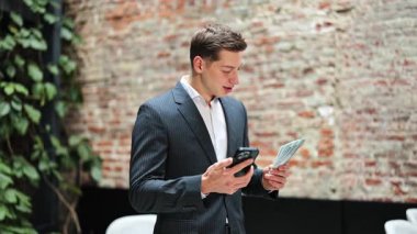 Takım elbiseli neşeli iş adamı telefon edip para sallıyor, modern ofiste başarıyı kutluyor. Heyecanlı ve mutlu hissediyor..