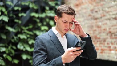 Takım elbiseli stresli işadamı akıllı telefondan rahatsız olur. Yatırımcı, uzman, resmi olarak erkek. Borsa haberleri başarısızlıkla sonuçlanıyor. Ofis koridorunda hüzünlü duygular.