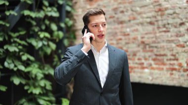 Takım elbiseli kendine güvenen bir işadamı akıllı telefondan konuşuyor. Profesyonel bir erkeğin ofisinde telefon görüşmesi var. İş, iletişim, teknoloji.