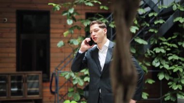Takım elbiseli kendine güvenen bir işadamı telefonda konuşuyor. Başarılı bir girişimci ofis avlusunda iş anlaşması yapıyor. Neşeli, anlaşma, başarı.