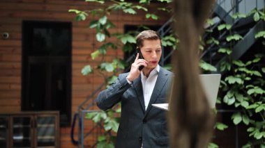 Kendine güvenen iş adamı dizüstü bilgisayar kullanıyor ve telefonda konuşuyor. Başarılı yatırımcı, şık bir ofiste uzaktan kumandalı olarak çalışır. Neşe, odaklanma, konsantrasyon.