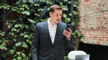Heyecanlı takım elbiseli iş adamı telefonla iyi haberler alıyor. Modern ofiste zaferi kutlayan başarılı bir girişimci. Neşe, başarı, iyi anlaşma..