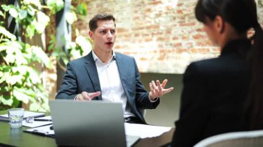 Profesyonel işadamı ve iş kadını modern ofiste belgeleri tartışıyor. Resmi olarak ciddi iş ortakları dizüstü bilgisayarla masada otururlar..