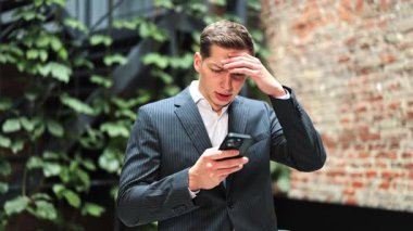 Takım elbiseli stresli işadamının ofis dışında telefon kullanması kötü haberler, iş sorunları veya olumsuz mesajlar karşısında hayal kırıklığına uğruyor.