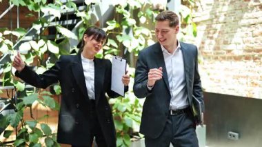 Şık takım elbiseli heyecanlı iş ortakları modern bir ofis salonunda dans ederek başarılarını kutluyorlar. Neşe, başarı ve motivasyon havayı doldurur..