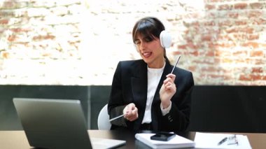 Resmi takım elbiseli mutlu iş kadını kulaklıkla müzik dinliyor ve modern ofiste but olarak kalem kullanıyor..