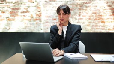 Ofiste diş ağrısı çeken takım elbiseli stresli bir iş kadını. Yanağına dokunuyor ve çok acı çekiyor..