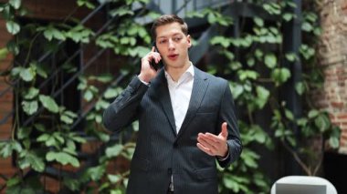 Modern bir ofiste takım elbiseli kendine güvenen bir işadamı telefonda konuşuyor. Görüşme sırasında başarılı ve ciddi görünüyor..