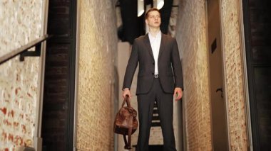 Seyahat çantası taşıyan takım elbiseli kendine güvenen iş adamı ofis koridorunda duruyor. Güven ve profesyonellik yayıyor..