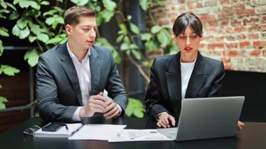 Resmi giyimde odaklanmış meslektaşlar ofiste dizüstü bilgisayarla bir projeyi tartışıyorlar. Hevesli iş ortakları belgelerle çalışır ve bilgiyi analiz ederler..