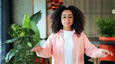 Neşeli Afrikalı Amerikalı iş kadını modern, yeşil bitki dolu bir ofiste güvenle gülümseyen gözlüğünü mutlulukla çıkarıyor. IT uzmanı başarılı ve hazır hissediyor.