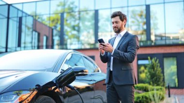 Akıllı takım elbiseli başarılı bir iş adamı, neşeli, telefonla iletişim kuran. Elektrikli araç lüks, modern ofis binası, modern sürdürülebilir seyahat sergisi. İş adamı mutlu..