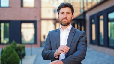 Sivri takım elbiseli mutlu profesyonel işadamı kollarını açık havada kavuşturarak duruyor. İnsanoğlu bu modern şehir ortamında neşeli bir gülümsemeyle başarı ve pozitiflik yayar..