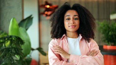 Pembe tişörtlü ve beyaz tişörtlü profesyonel Afro-Amerikan iş kadını modern ofis içinde kendine güvenen biri. Kız sakince gülümsüyor, başarıyı ve olumlu refahı yansıtıyor..