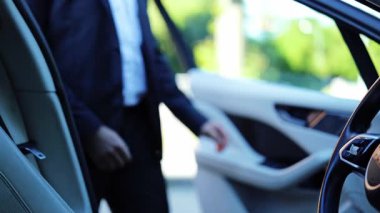 Koyu takım elbiseli başarılı bir işadamı lüks bir arabaya biner. Profesyonel erkek sakince yerleşir, ellerini direksiyona koyar, kendinden emin sürüş için hazırlanır. Günlük işe gidiş gelişi temsil eder.