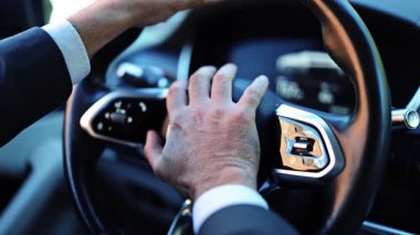 Modern bir arabanın içindeki profesyonel iş adamı, koyu renk bir takım giymiş, sabırsızlıkla kornaya basıyor. Onun eylemleri trafik sırasında hayal kırıklığını iletir.