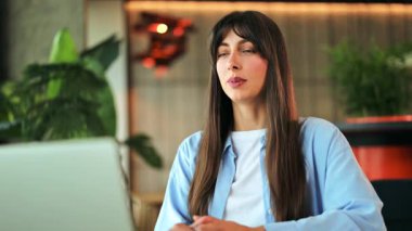 Mavi tişört ve beyaz tişört giyen kendine güvenen profesyonel iş kadını, modern bir çalışma alanında dizüstü bilgisayarla aktif bir şekilde iletişim kuruyor, meşgul ve verimli hissediyor..