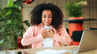 Ofis masasında oturan endişeli Afrikalı Amerikalı kadın göğüs rahatsızlığı ve nefes almakta güçlük çekiyor. Göğsünü acı içinde tutuyor. Endişe ve sıkıntı belirtileri gösteriyor..