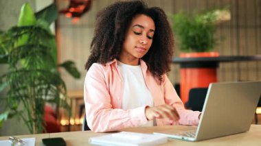 Pembe gömlekli sakin bir Afro-Amerikan kadın, modern bir ofiste dizüstü bilgisayar çalışmalarına ara veriyor. Gözlerini kapatıyor, yoğun gününün ortasında bir farkındalık ve huzur dolu bir rahatlama anı buluyor..