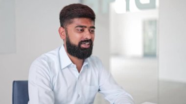 Açık mavi gömlekli profesyonel Hintli işadamı, parlak bir ofiste planlarını tartışır, sohbet sırasında olumlu duygular ve uzmanlık aktarır..