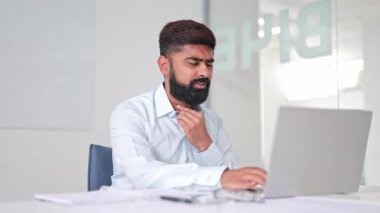 Beyaz gömlekli hasta Hintli işadamı, modern bir ofiste dizüstü bilgisayarla çalışırken boğaz rahatsızlığı yaşıyor. Odaklanma konusunda uzman olmayan girişimler.