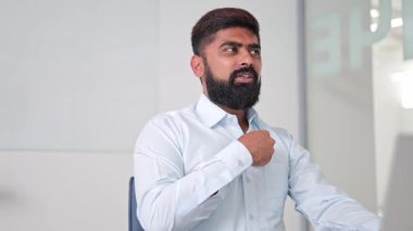 Açık mavi gömlekli profesyonel Hintli işadamı bir ofis toplantısı sırasında düşünceli ve konsantre görünüyor. İş yerinde bir yansıma ve odaklanma anı.