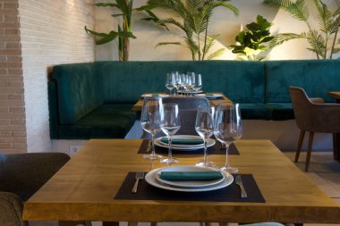 Yeşil kanepeli bir restoran yeşil peçeteli ve çatallı bir masa. Masada iki şarap bardağı ve iki tabak var.