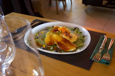 Masanın üzerinde yeşil bir peçete olan bir tabak yemek. Tabakta bir parça et, bir sebze ve bir sos da dahil olmak üzere çeşitli yiyecek ürünleri var.