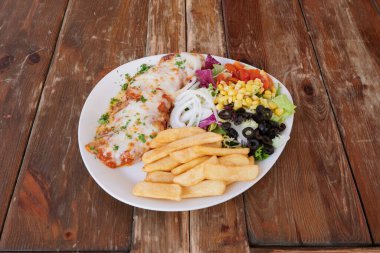 Bir tabak et, bir tabak patates kızartması ve bir salata. Tabak ahşap bir masanın üzerinde.