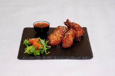 Bir tabak tavuk kanadı ve yanında salata. Tavuk kanatları baharatlı ve lezzetli görünüyor. Salata taze ve renkli, çeşitli yeşillikler ve domateslerle.