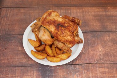 Tahta bir masada bir tabak tavuk ve patates. Tavuk pişti ve cildi çıtır çıtır. Patatesler dilimlenir ve tuz ve biberle tatlandırılır.