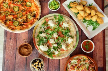 Çeşitli pizza çeşitleri ve diğer yiyecek maddelerinin olduğu bir masa. Olay yeri gündelik ve davetkar. Sanki aile ya da arkadaşlar bir yemeği paylaşıyor gibi.