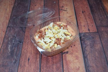 Üstünde kapağı olan bir konteynır dolusu yiyecek. Kapağı plastik, kabı da temiz. Konteynırın içindeki yemek pastırma ve yumurtalı bir salata.