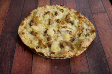 Peynirli ve etli bir pizza ahşap bir masada oturur. Pizza altın kahverengidir ve kıtır kıtır kıtır olur. Peynir eritilir ve et baştan sona pişirilir. Pizza çok lezzetli görünüyor.