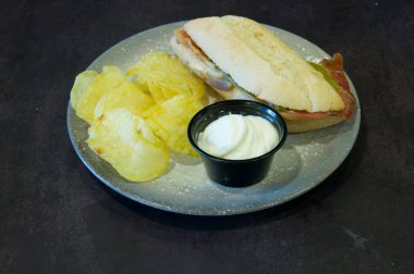 Üzerinde sandviç ve patates kızartması olan bir tabak. Sandviç ikiye bölünmüş ve cipsler sarı.